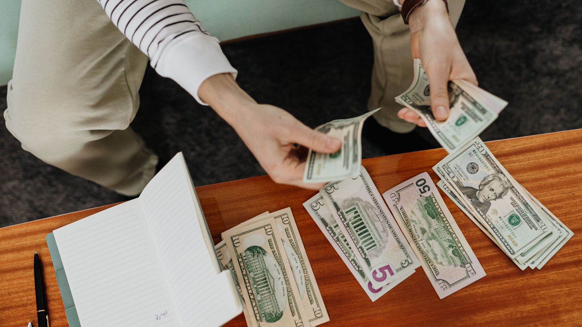A person sitting and counting various US dollar bills at a table indoors.