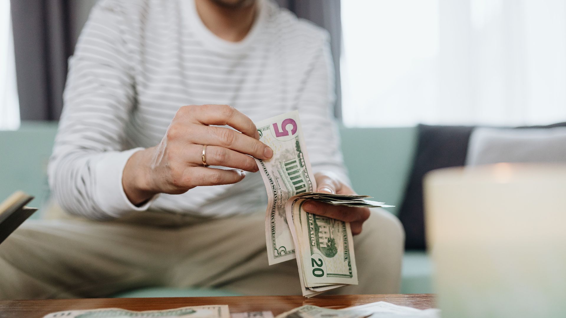 Close-up of hands counting dollar bills indoors, offering a personal finance theme.