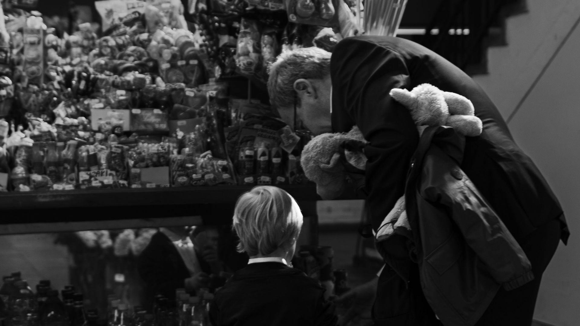 A grayscale image of a father and son browsing toys at a store counter indoors.