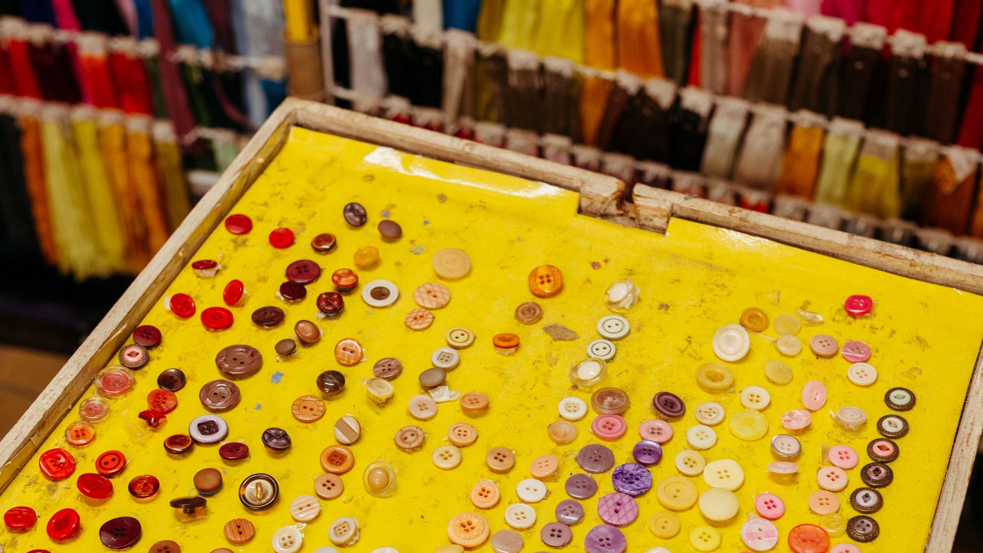 Vibrant collection of multicolor buttons displayed on yellow background in a fabric store.