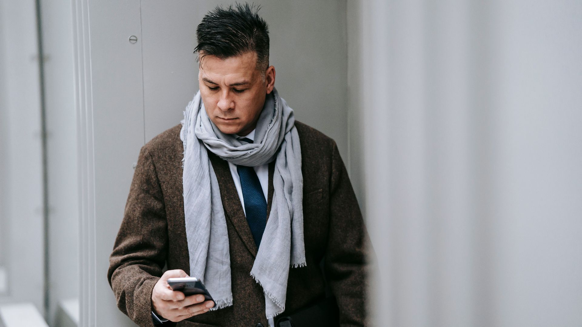 Professional man in a stylish coat and scarf using a smartphone outdoors, representing modern connectivity.