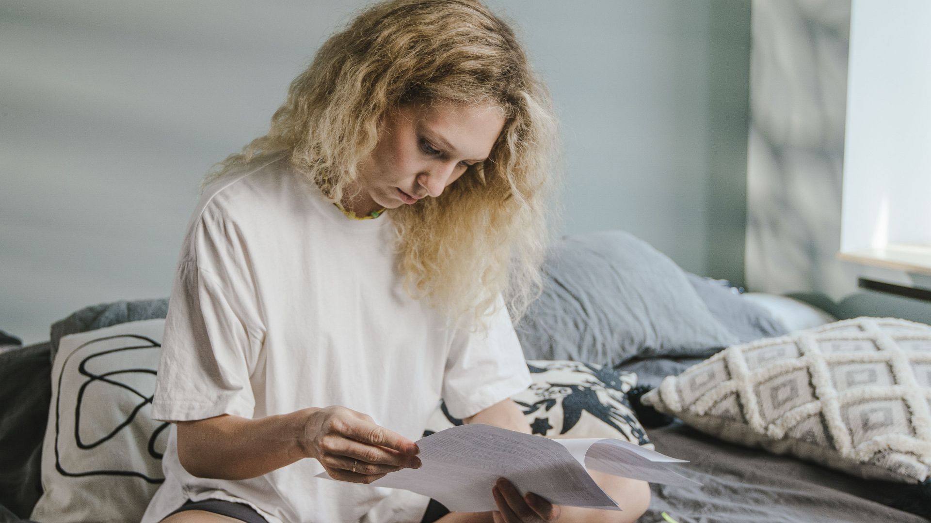 A woman working from home with a laptop and papers on her bed, enhancing comfort and productivity.