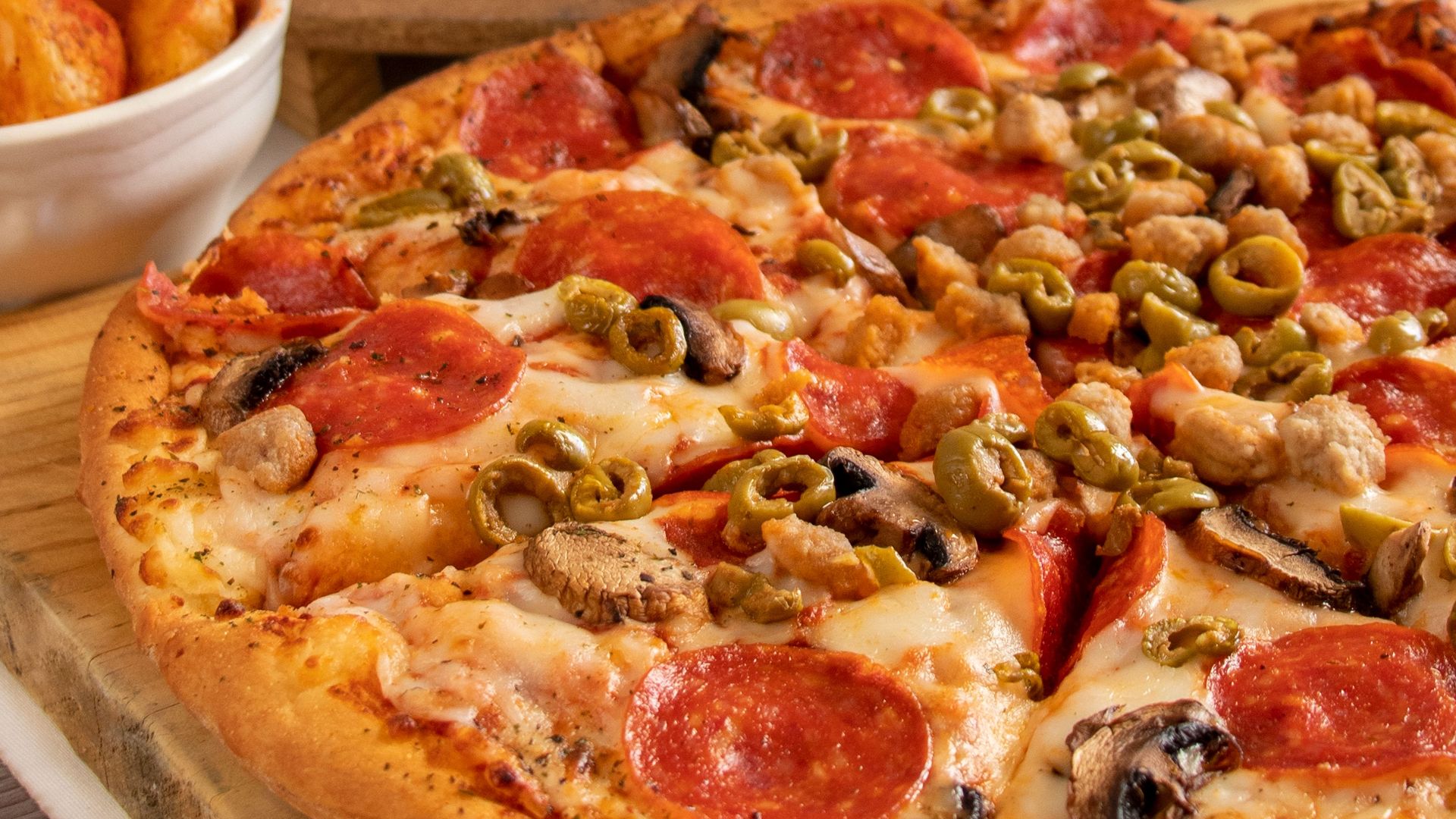 Appetizing pepperoni pizzas with mixed toppings and drinks on a table.