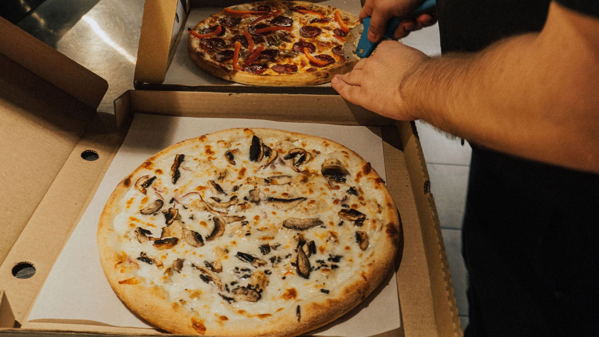 A chef cuts freshly baked pizzas ready for delivery in a busy restaurant kitchen.