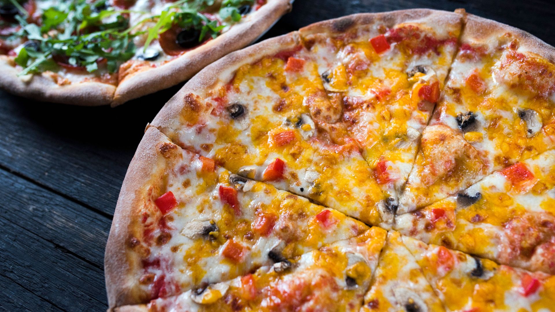 High angle of yummy pizzas with vegetable and mushroom slices on melted cheese on dark background