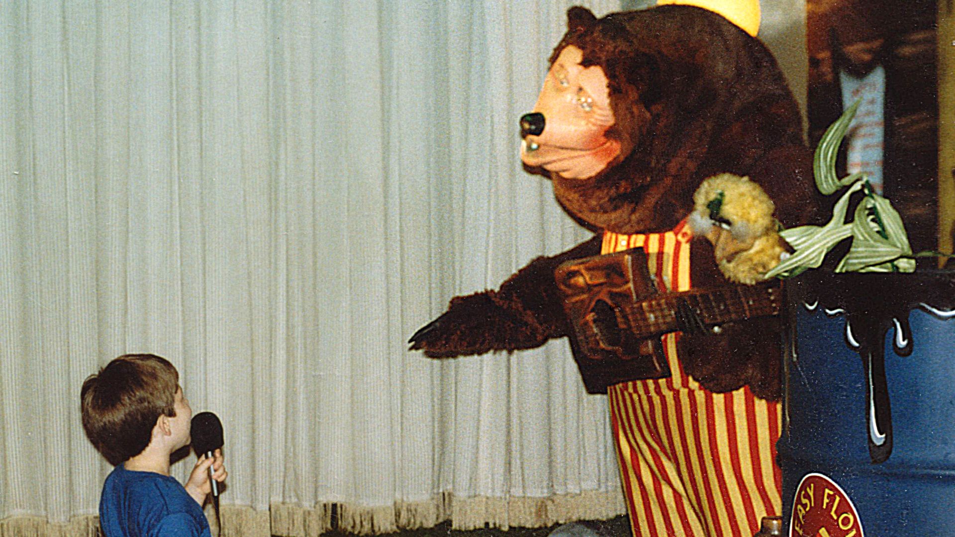 A child uses a microphone to speak to Billy Bob, mascot of ShowBiz Pizza Place, during a birthday party at ShowBiz Pizza in Fayetteville, Arkansas.  The child is Ben Schumin, i.e. User:SchuminWeb.
