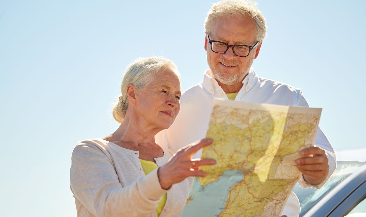 road trip, travel and old people concept - senior couple at car looking for location on map in summer