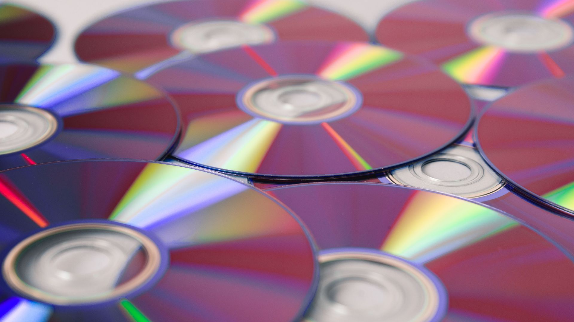 Stack of colorful CDs reflecting light, showcasing vibrant refractions and round patterns.