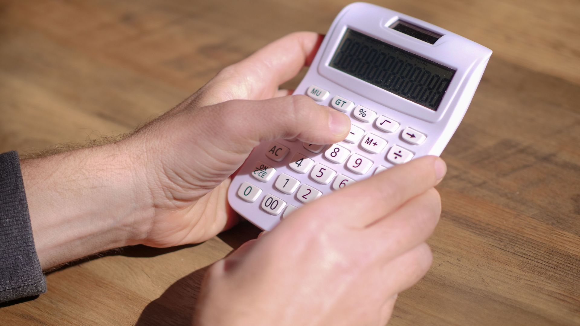 Hands using a pink calculator on a wooden table, emphasizing calculation and mathematics.