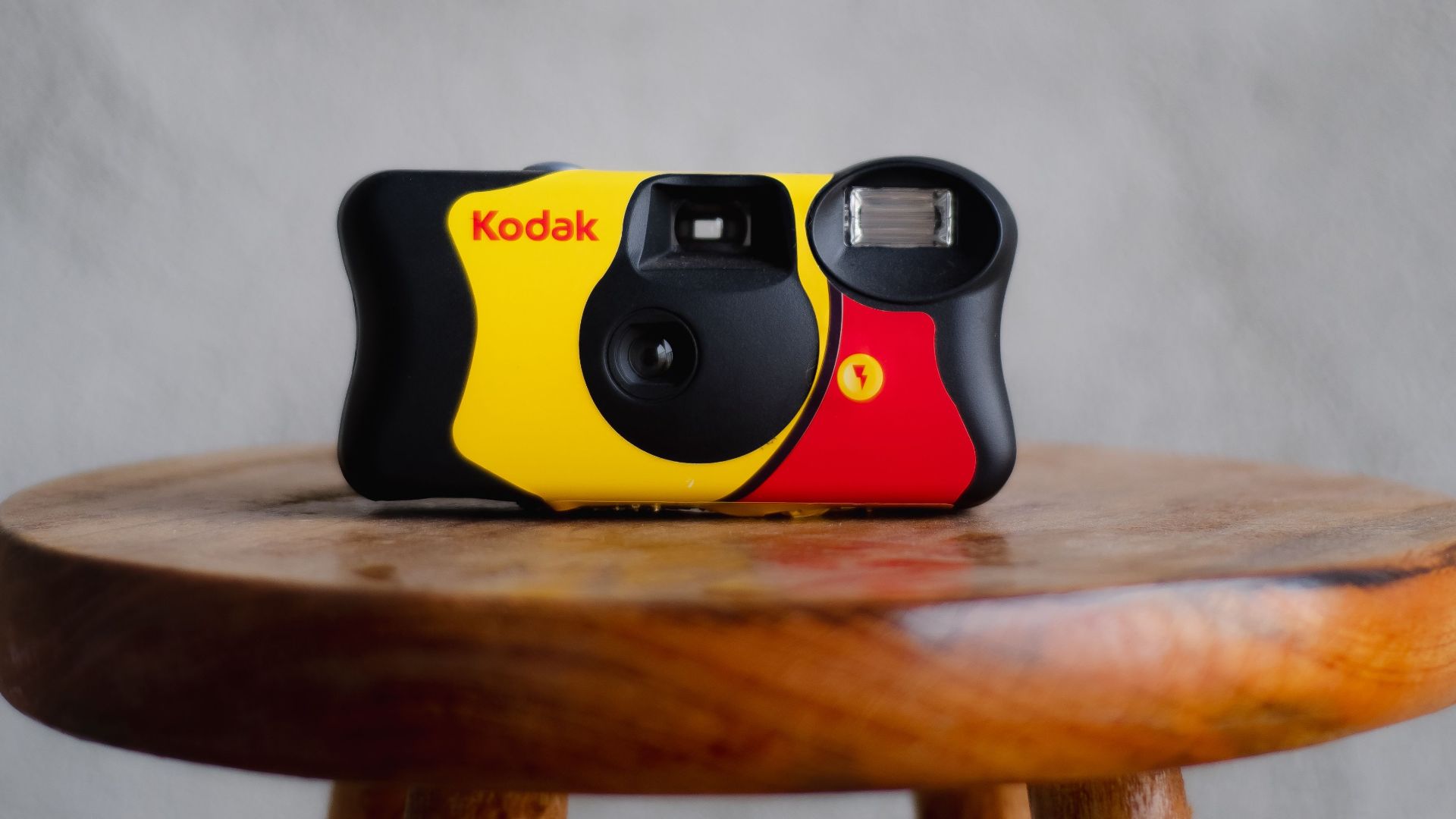 A classic Kodak film camera sitting on a wooden stool with a grey background.