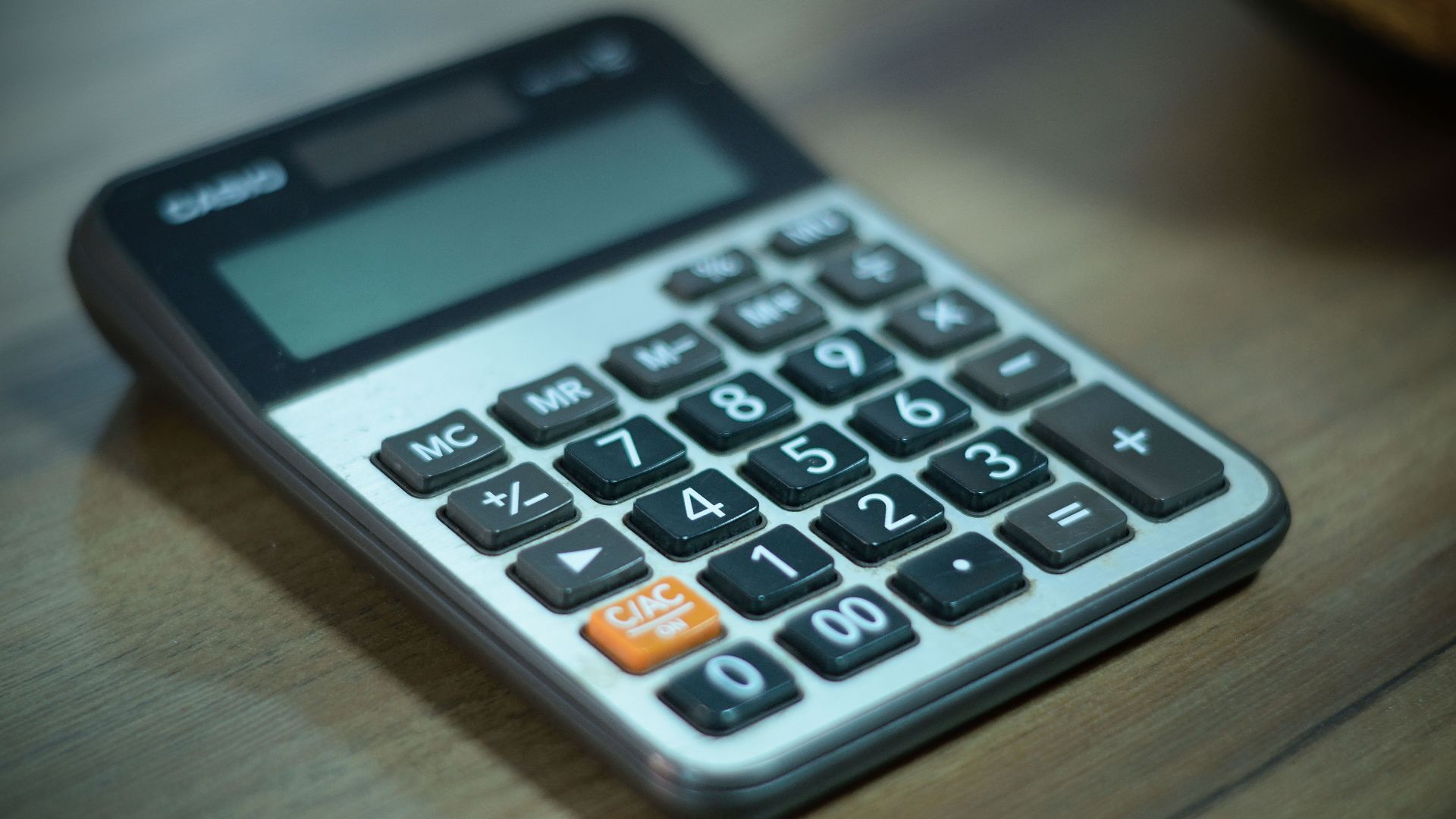 Digital calculator resting on a wooden table, selective focus.