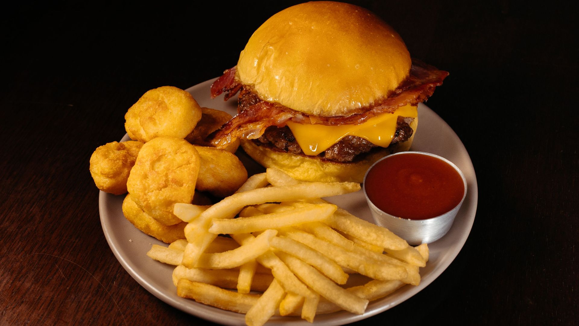 Tasty cheeseburger with bacon, fries, and nuggets on a plate with ketchup sauce.