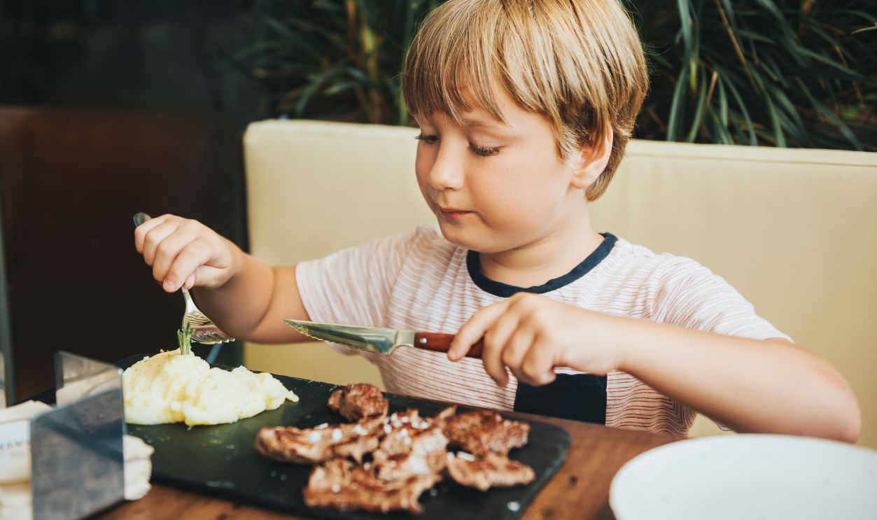 Cute little boy eating steak and mashed potatoes in the restaurant