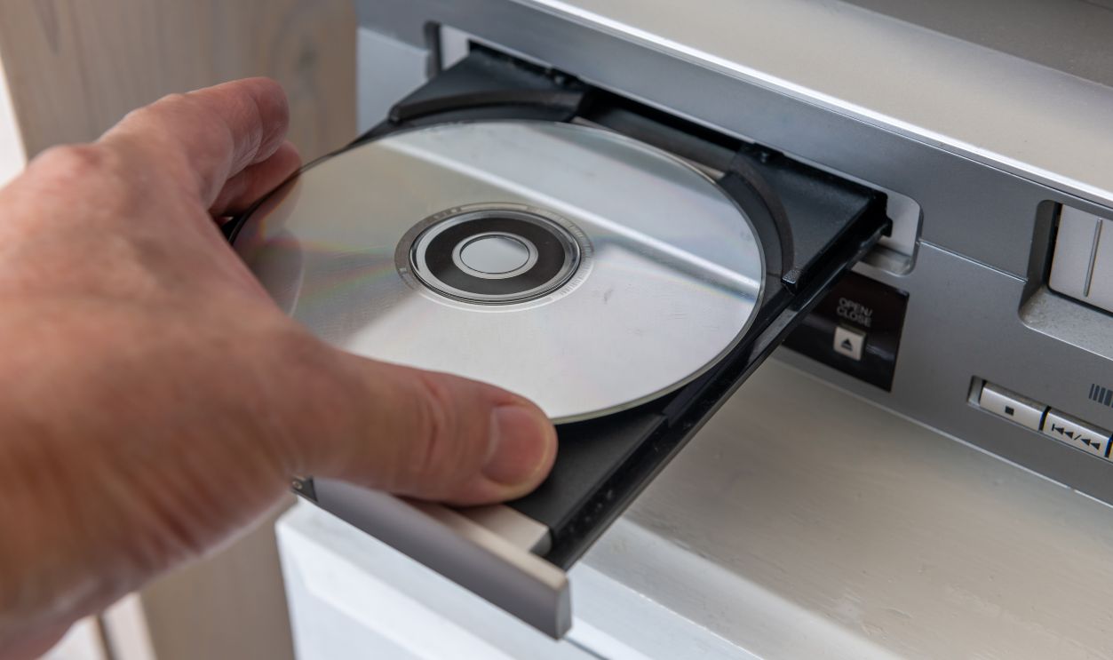 A person inserting a digital video disc into a DVD player.