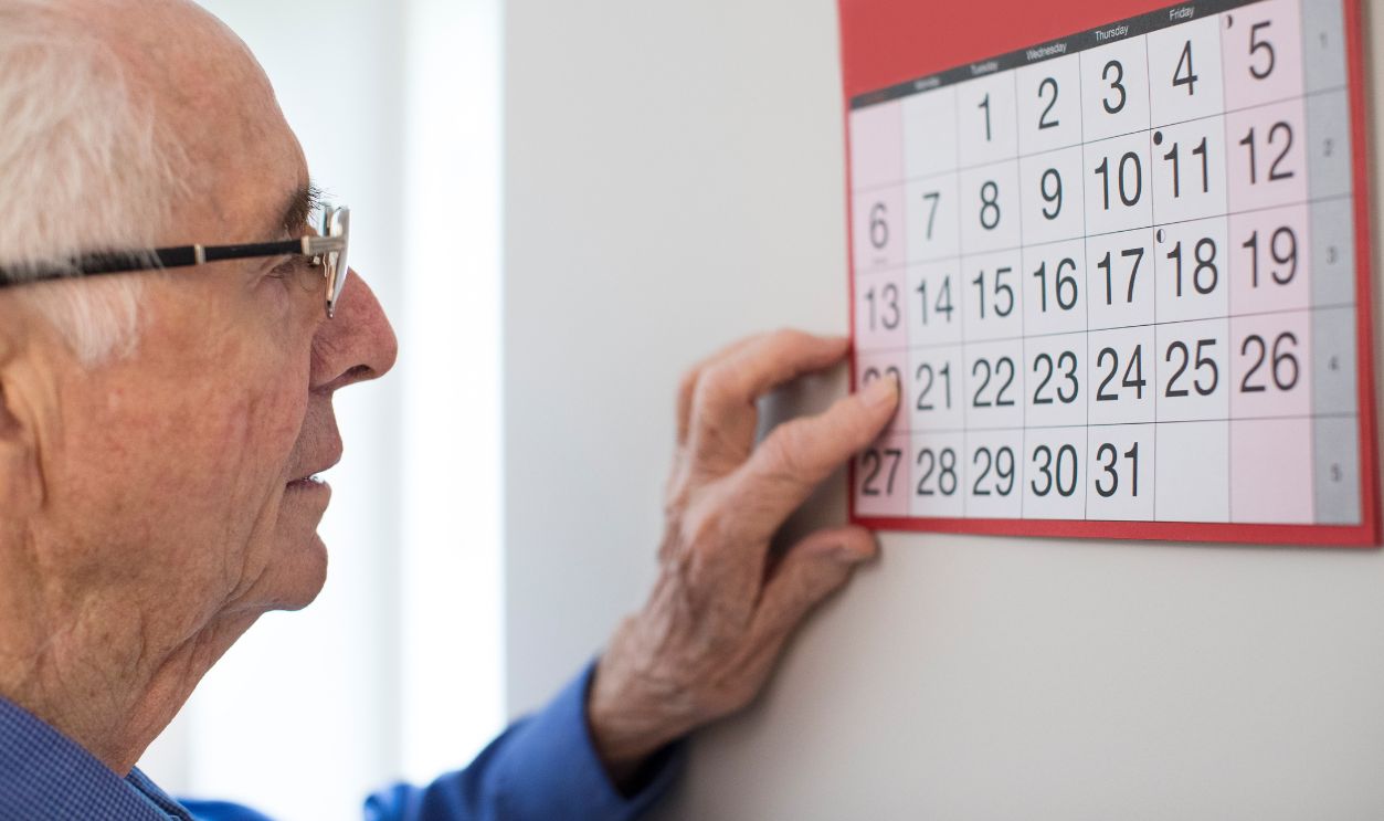 Confused Senior Man With Dementia Looking At Wall Calendar