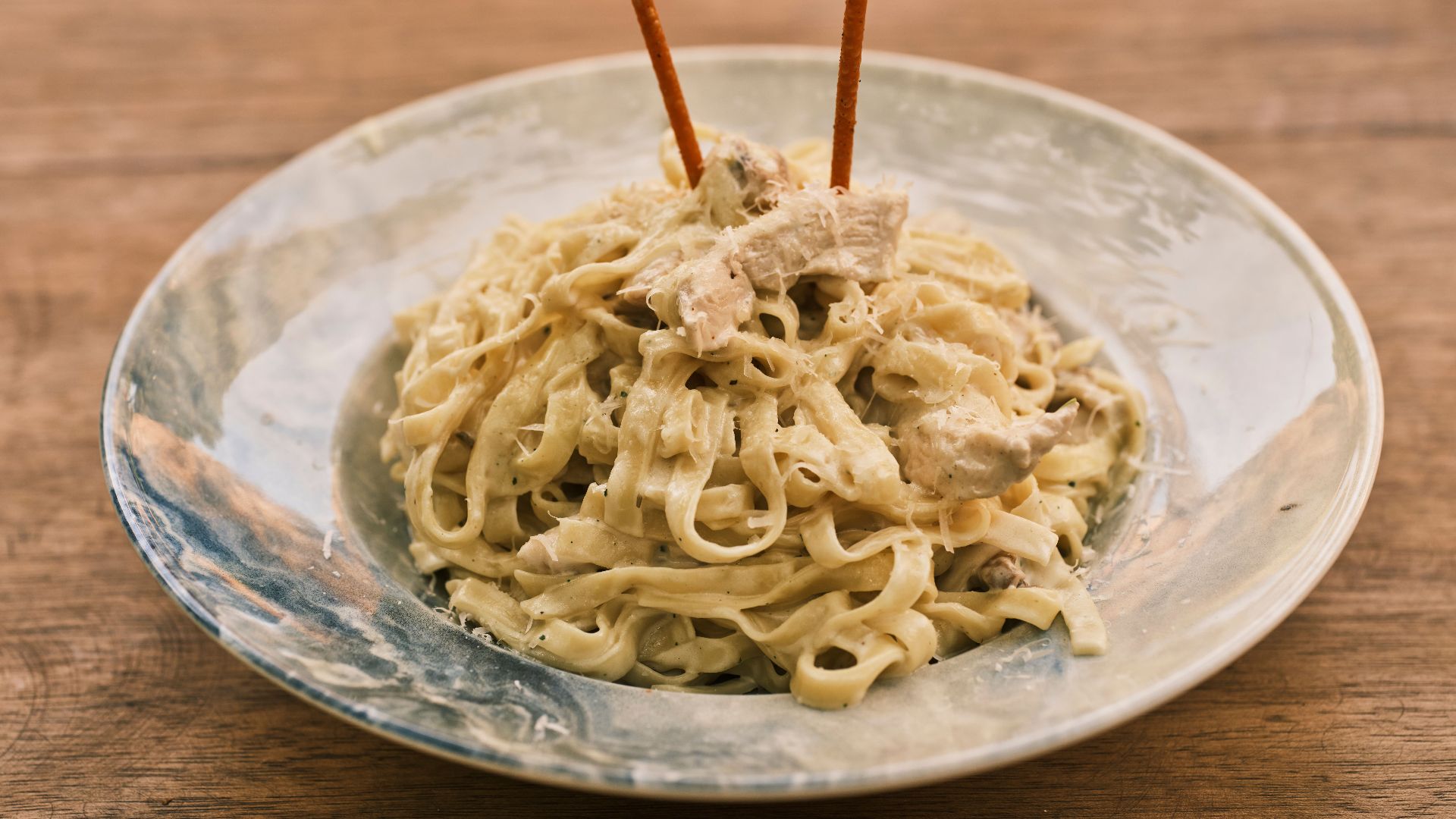 Delicious fettuccine alfredo with chicken on a rustic wooden table.