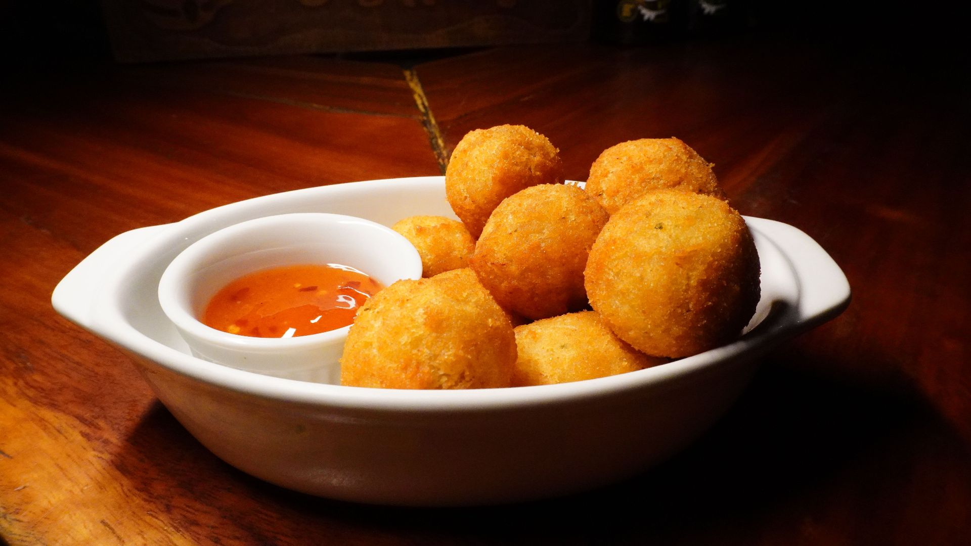 Golden brown cheese balls served with spicy dip in white bowl on wooden table.