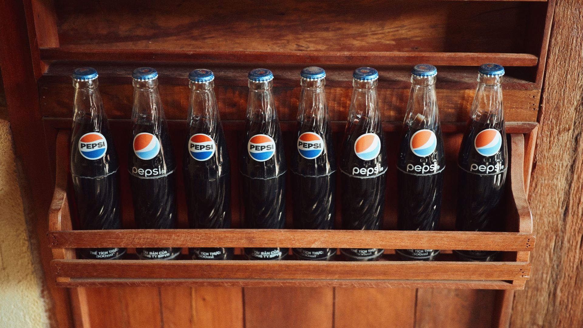A collection of vintage Pepsi bottles showcased in a rustic wooden rack.