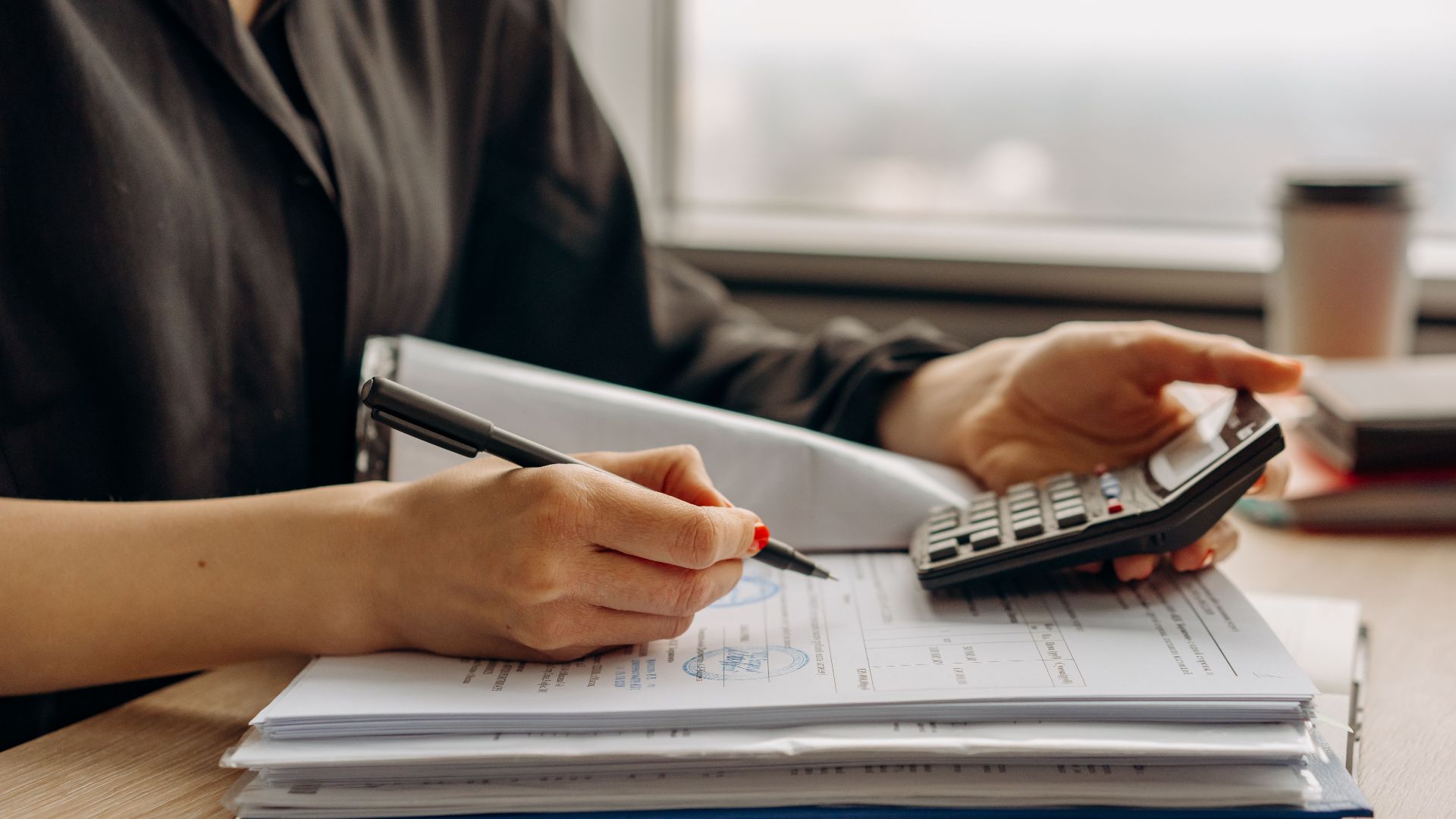 Close-up of person using a calculator with financial documents in an office.