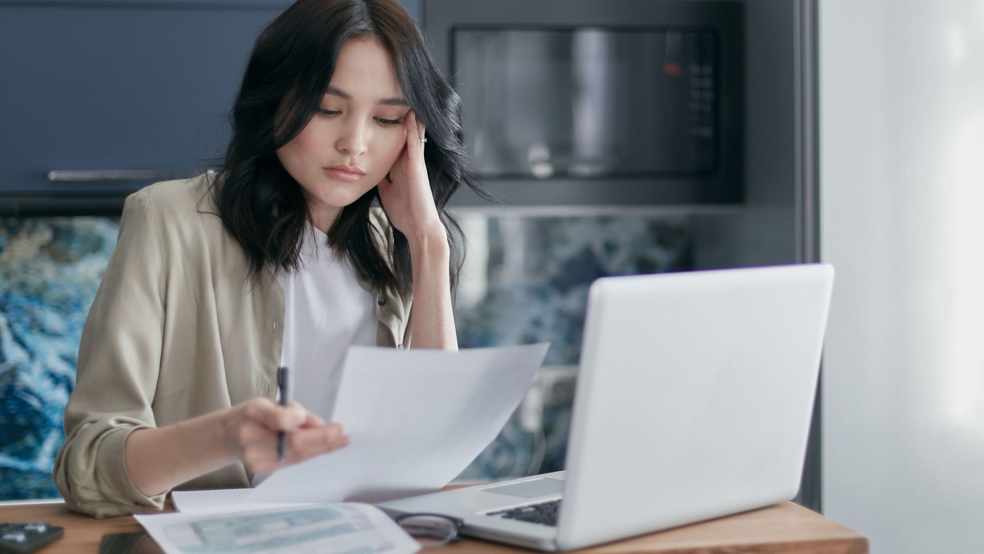 Focused young woman reviewing financial documents with a laptop in a home office setting.