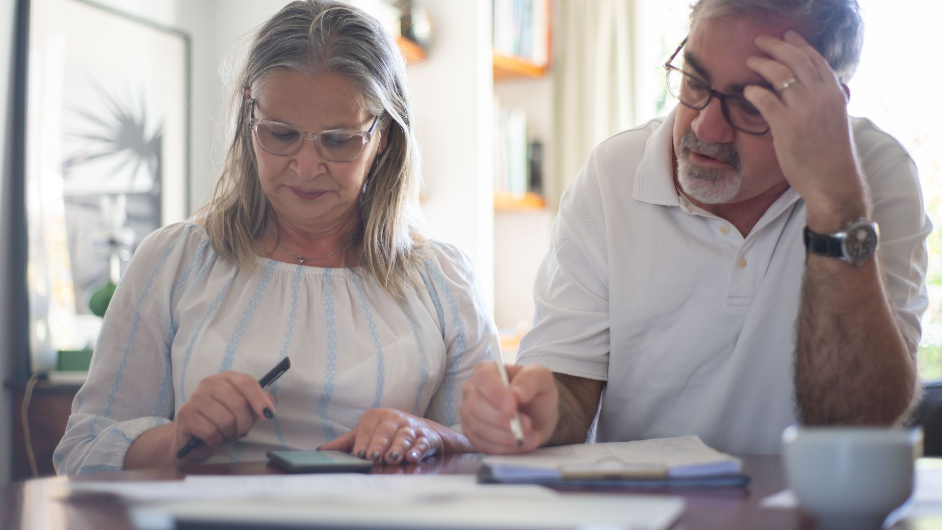 Senior couple calculating expenses at home office desk with documents and notes.