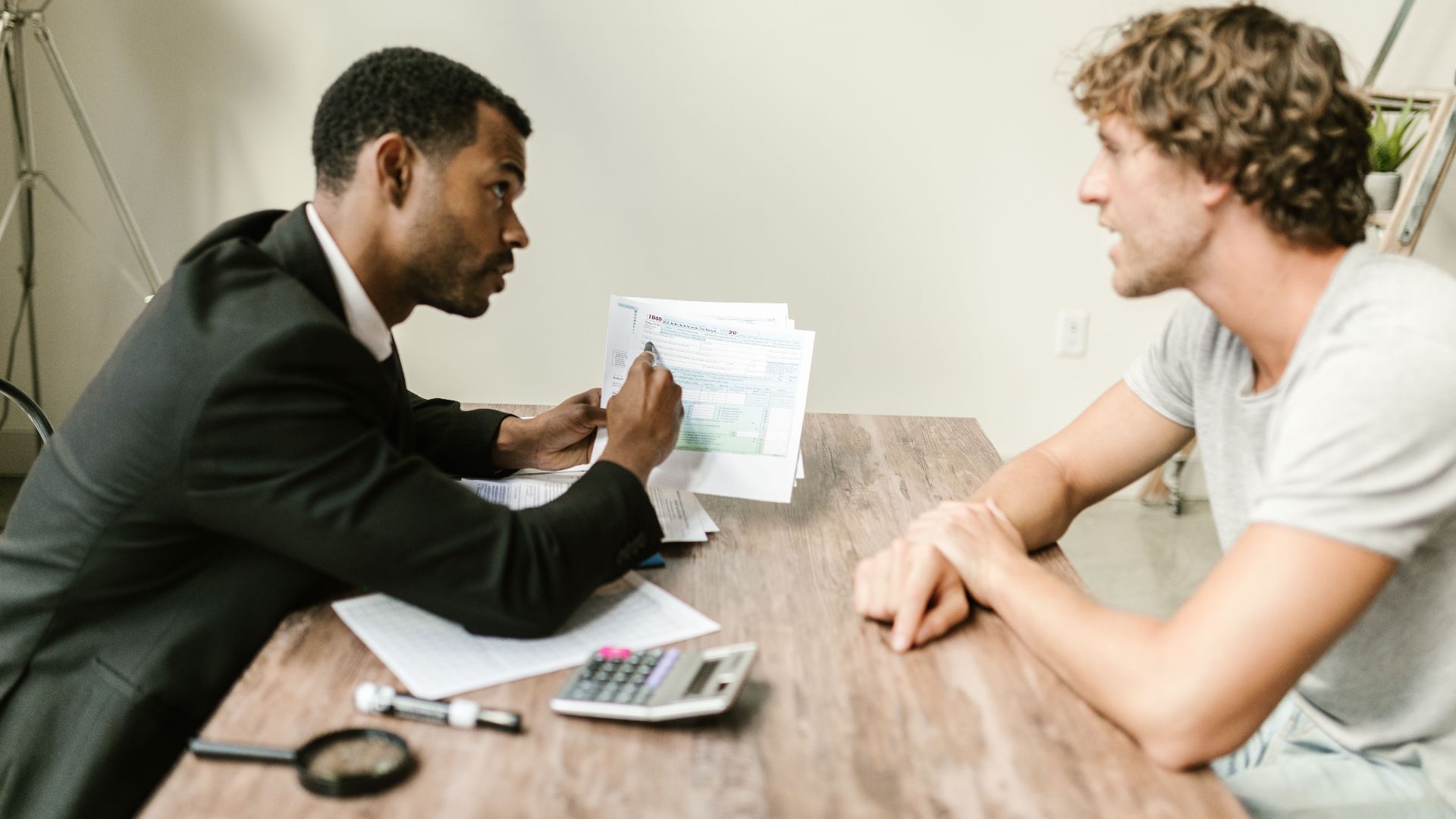 A financial advisor discusses paperwork with a client at a desk in a modern office.