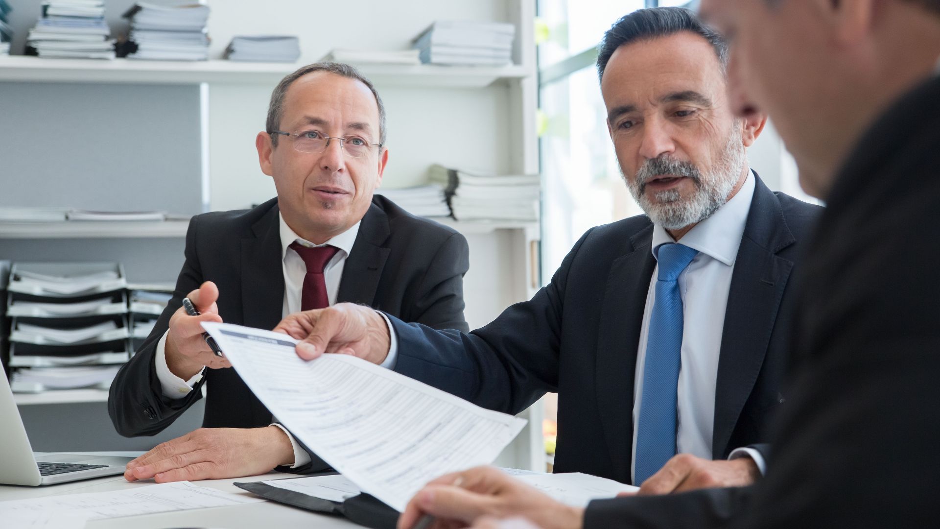 Three businessmen discussing documents in a modern office setting.
