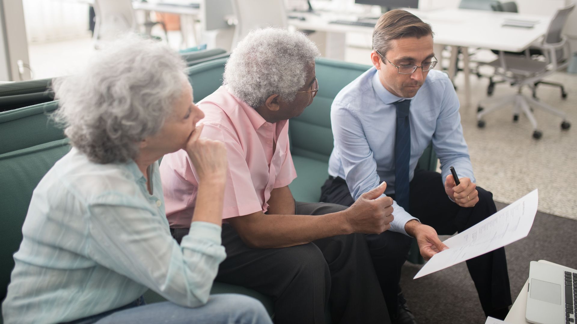 Business professional consults elderly clients in an office setting. Collaborative discussion, paperwork visible.