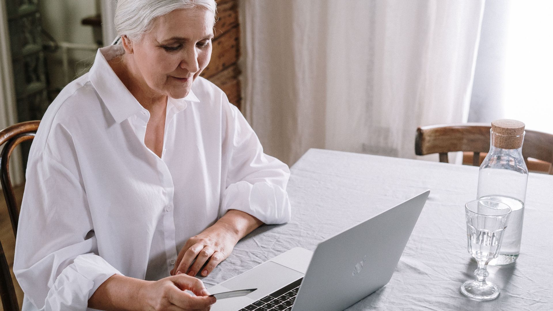 Elderly woman using laptop for online shopping at home during daytime.