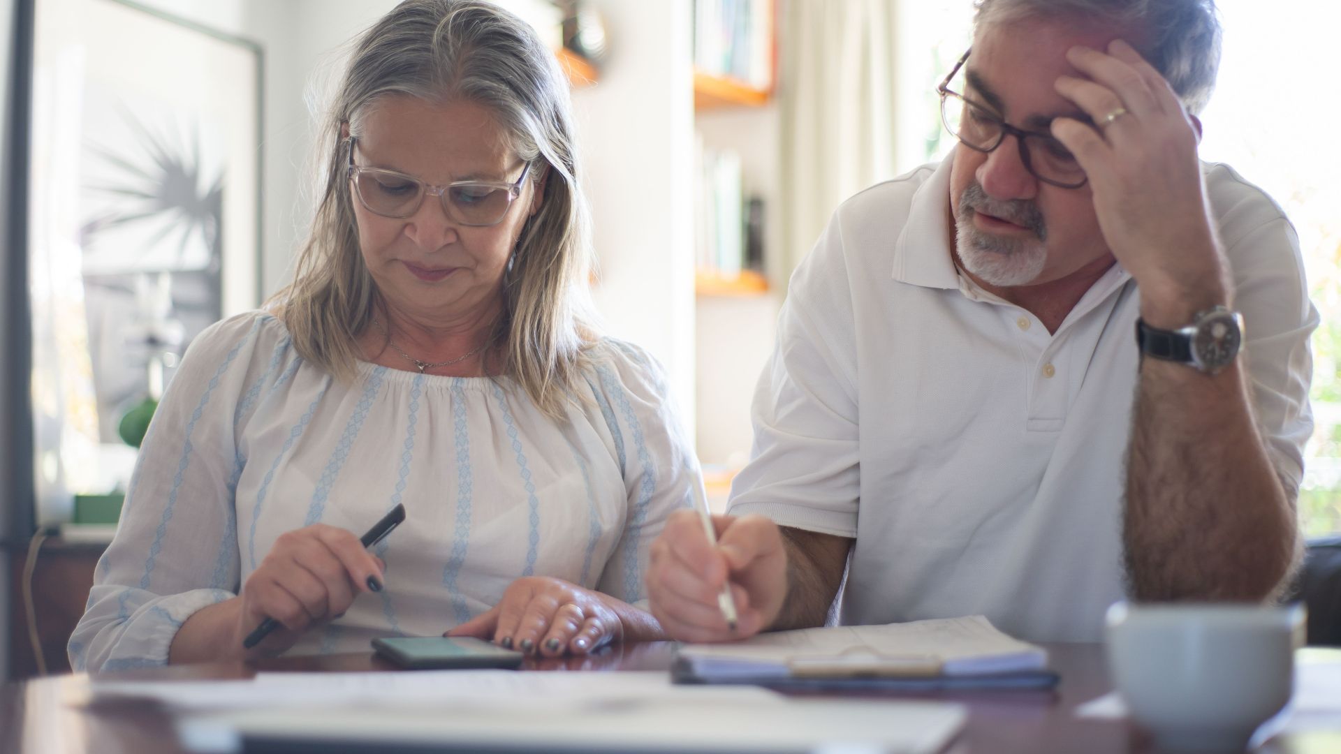Senior couple calculating expenses at home office desk with documents and notes.
