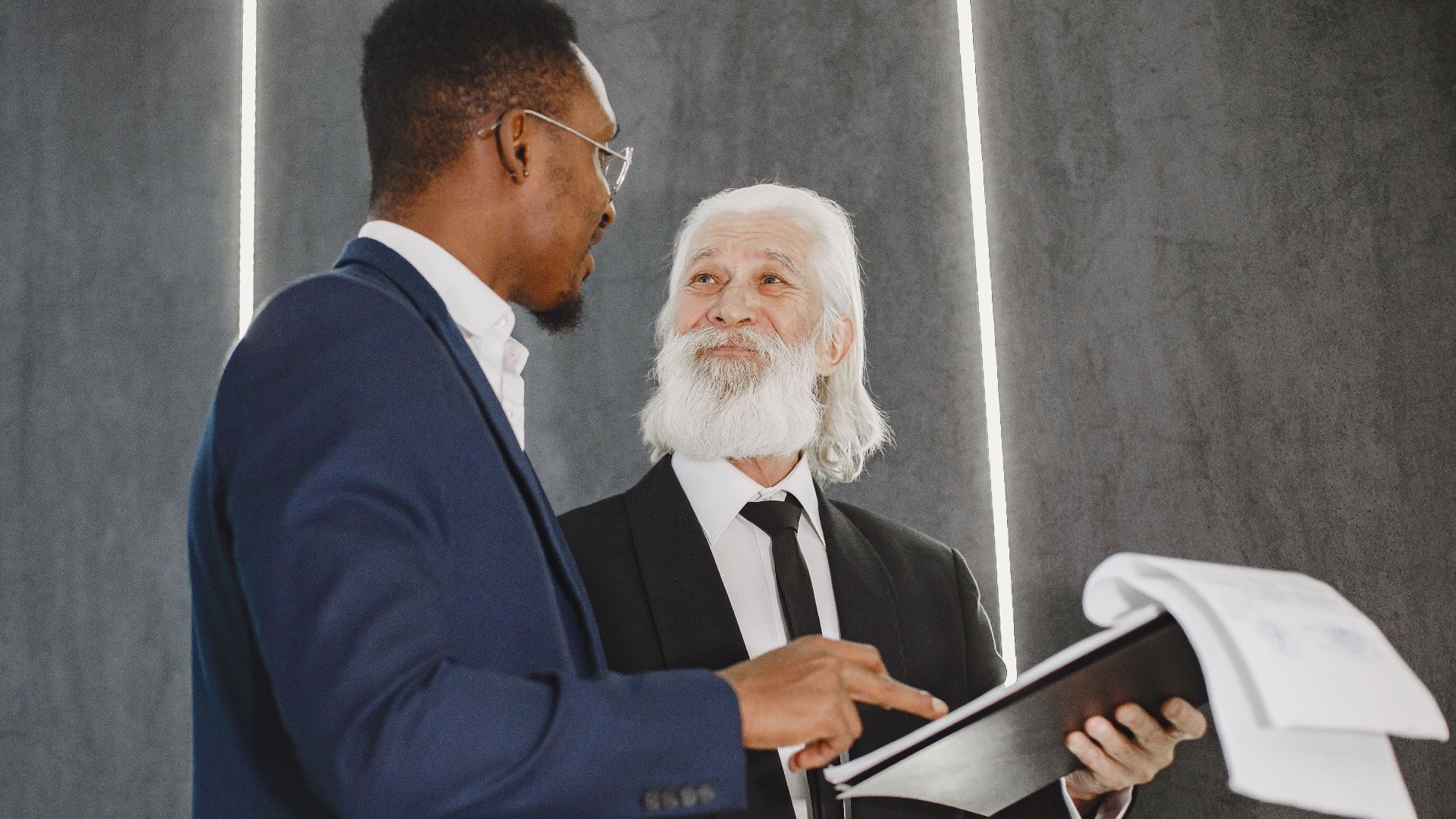 Two businessmen discussing documents in a modern office setting, highlighting professional diversity.