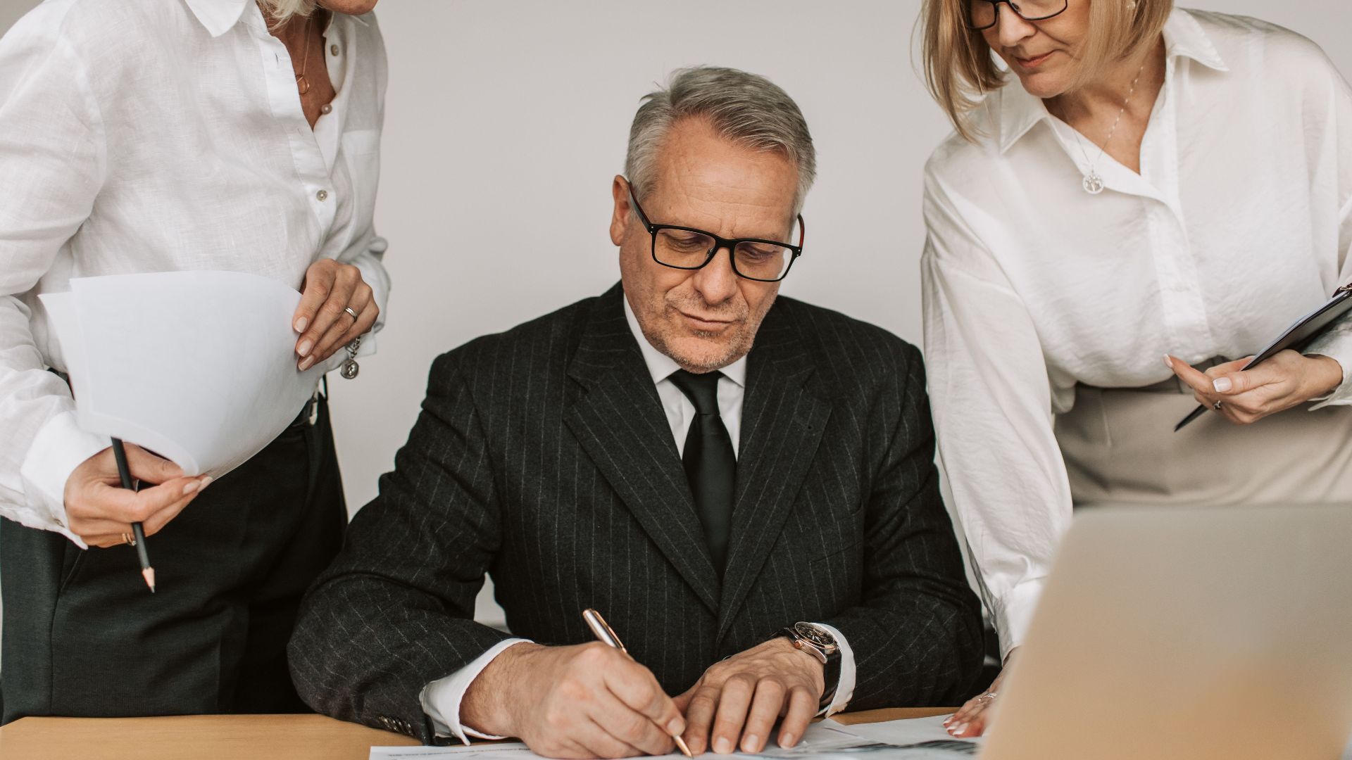 Senior professionals in an office setting reviewing and signing business documents together.