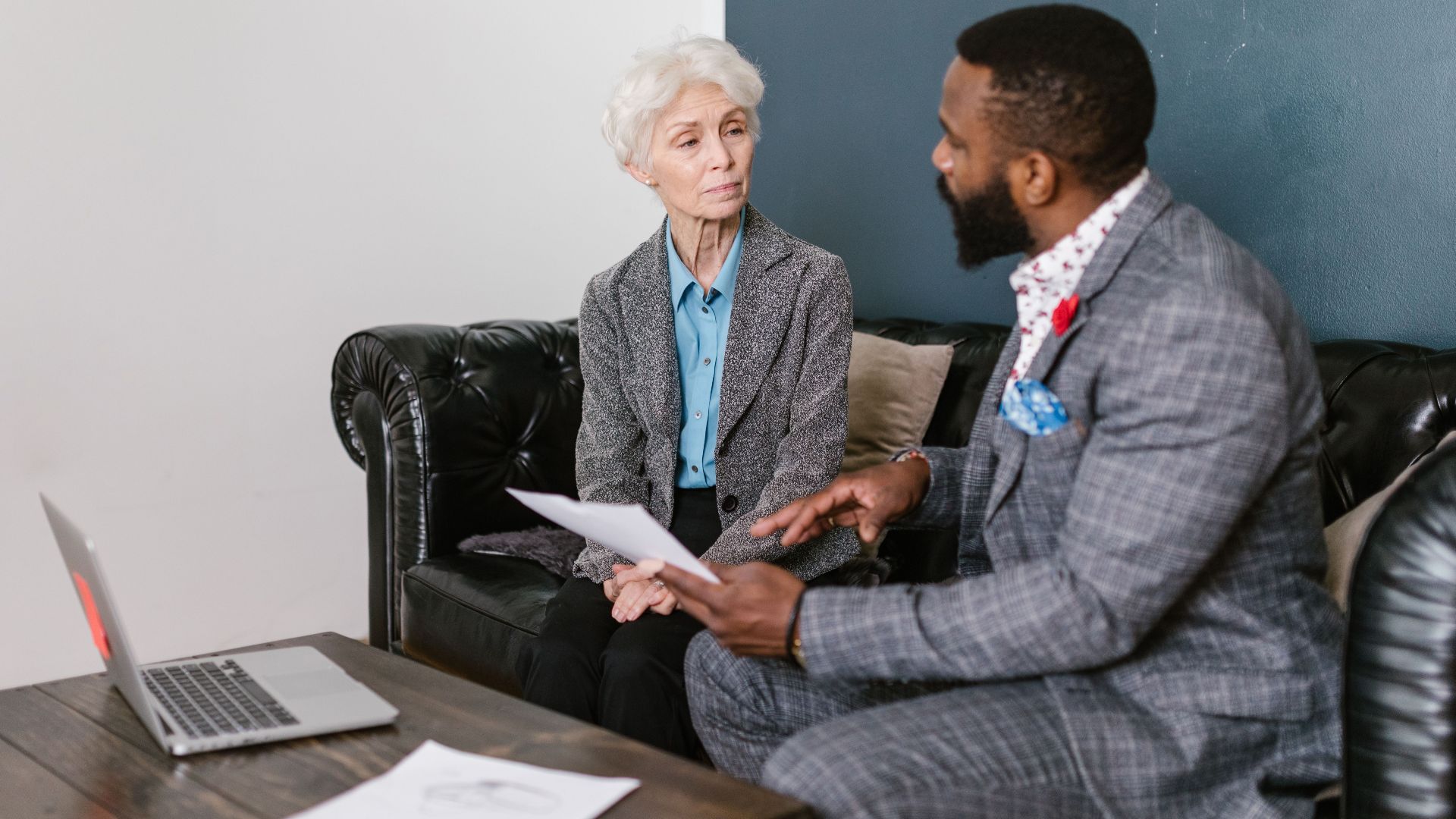 An elderly woman and a man in a professional meeting discussing documents indoors.