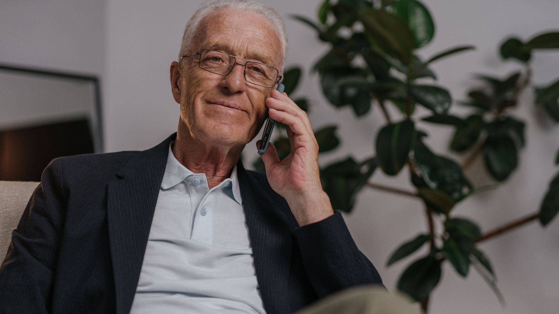 Elderly man with glasses making a phone call indoors, showing relaxed mood.