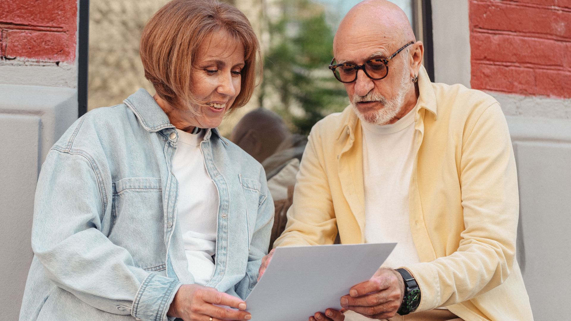 Elderly couple reading a document together while sitting outside at a cafe.