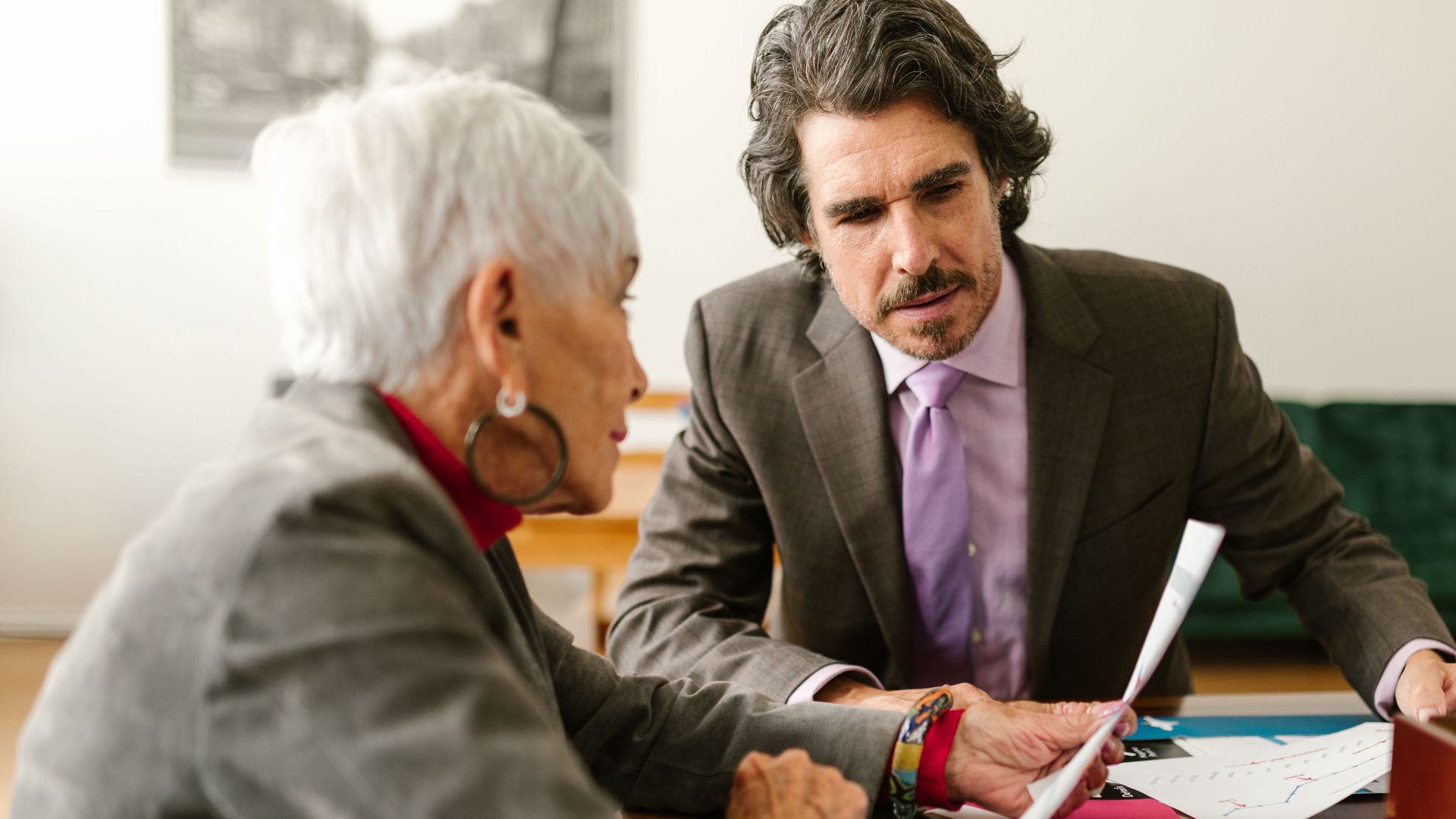 Elderly business professionals discussing reports in a modern office setting.