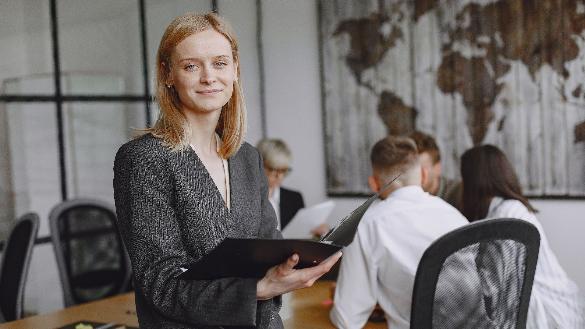 Confident businesswoman holding folder during a team meeting in modern office setting.