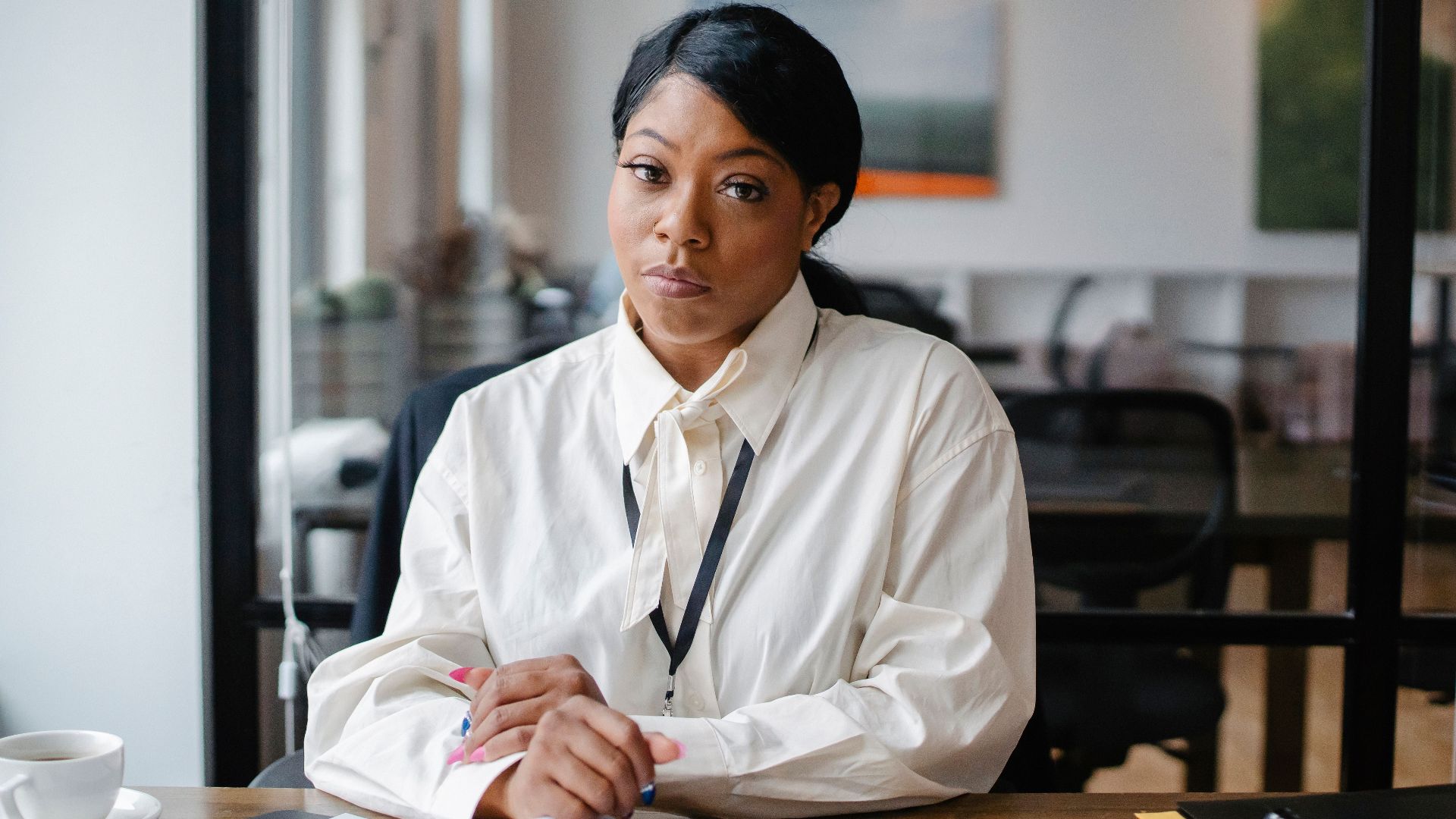 Calm African American businesswoman in formal outfit sitting at desk with papers in modern office and looking at camera