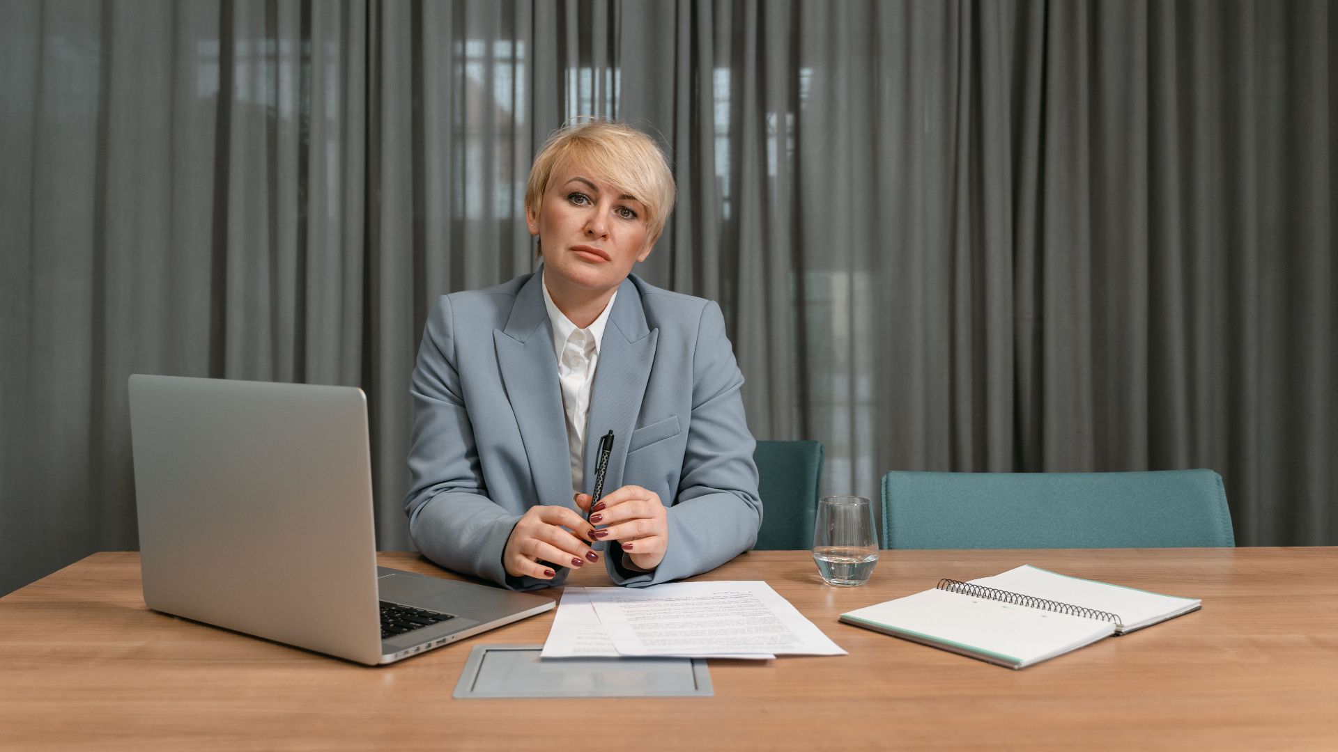 A confident businesswoman with short hair sits at a desk in a modern office environment.
