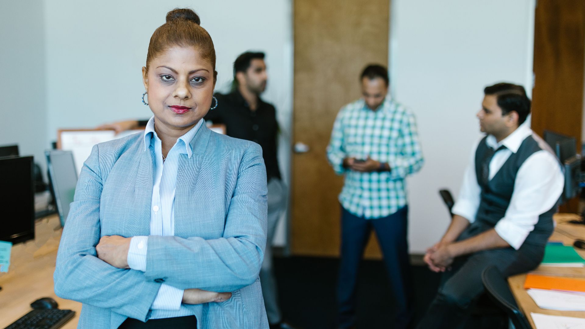 Confident businesswoman standing in modern office with colleagues in the background.