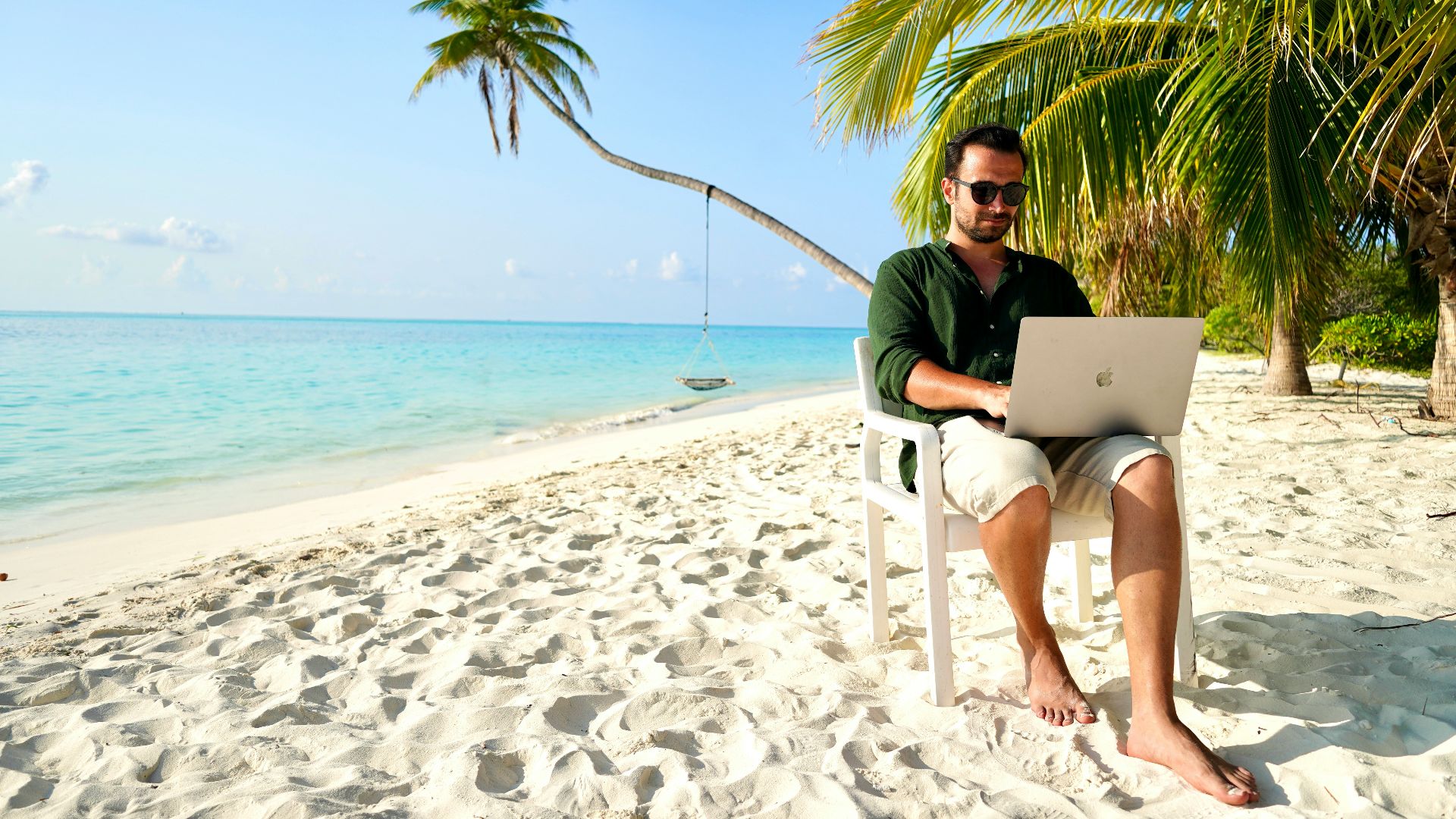 a man sitting in a chair on a beach using a laptop
