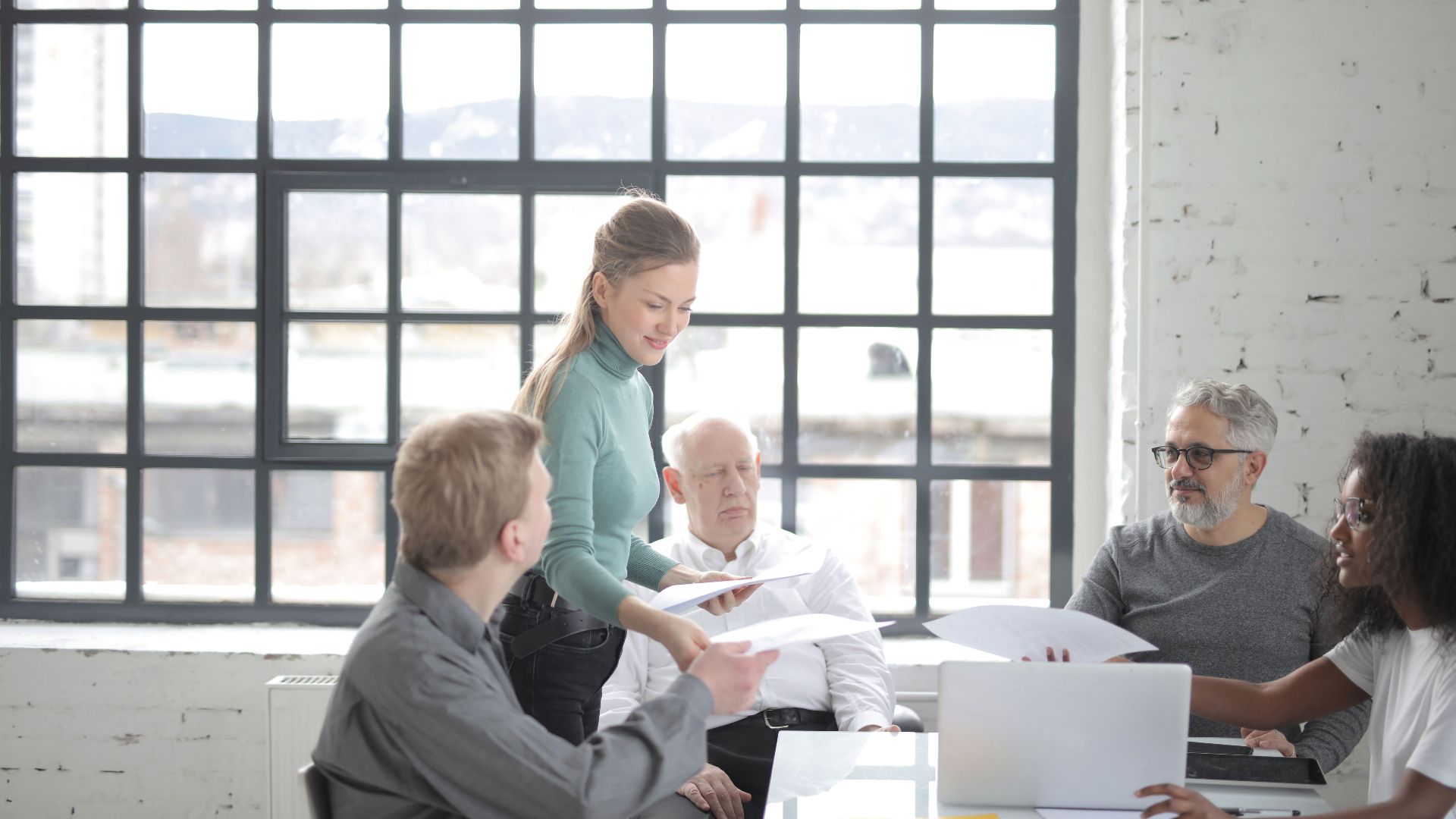 Multiracial coworkers of different ages in casual clothes discussing work plan and current issues at table with laptop in office