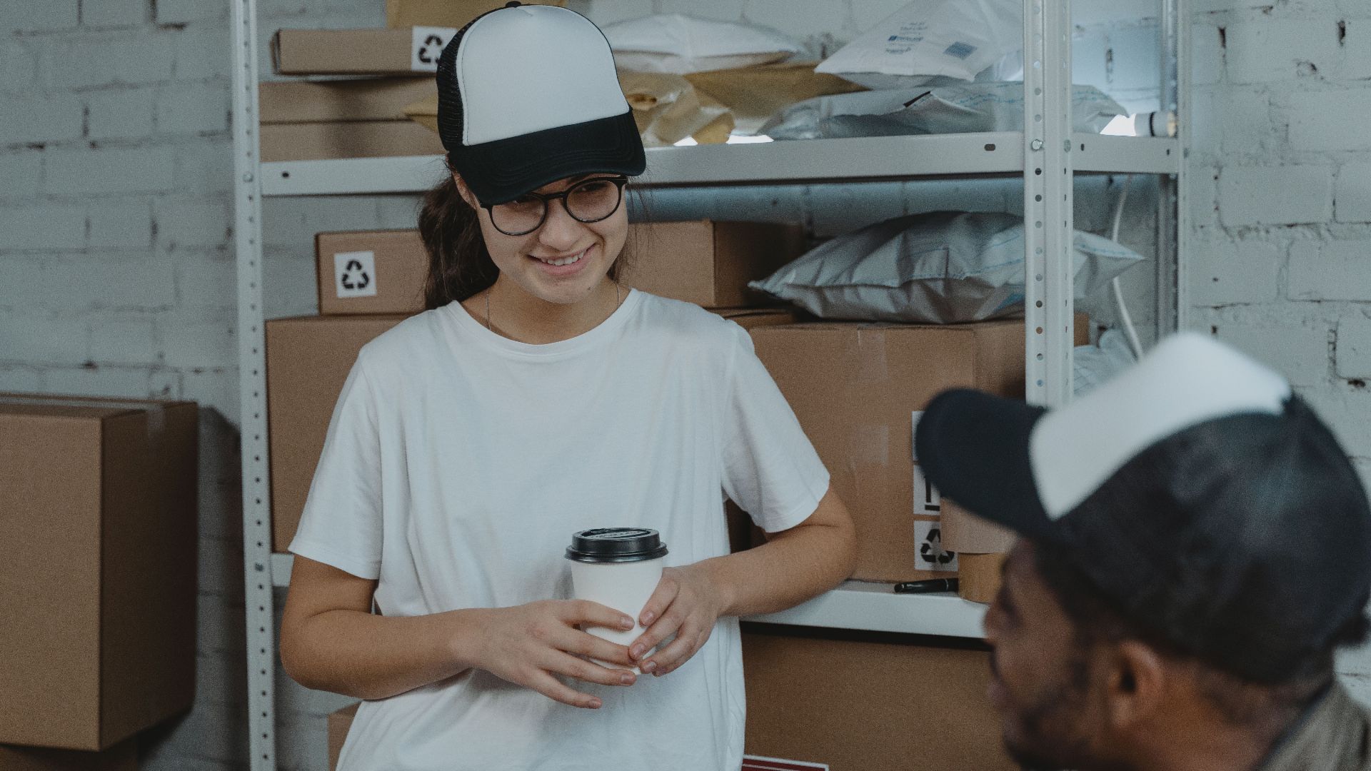 Two employees having a break and chatting in a warehouse, surrounded by packages and boxes.