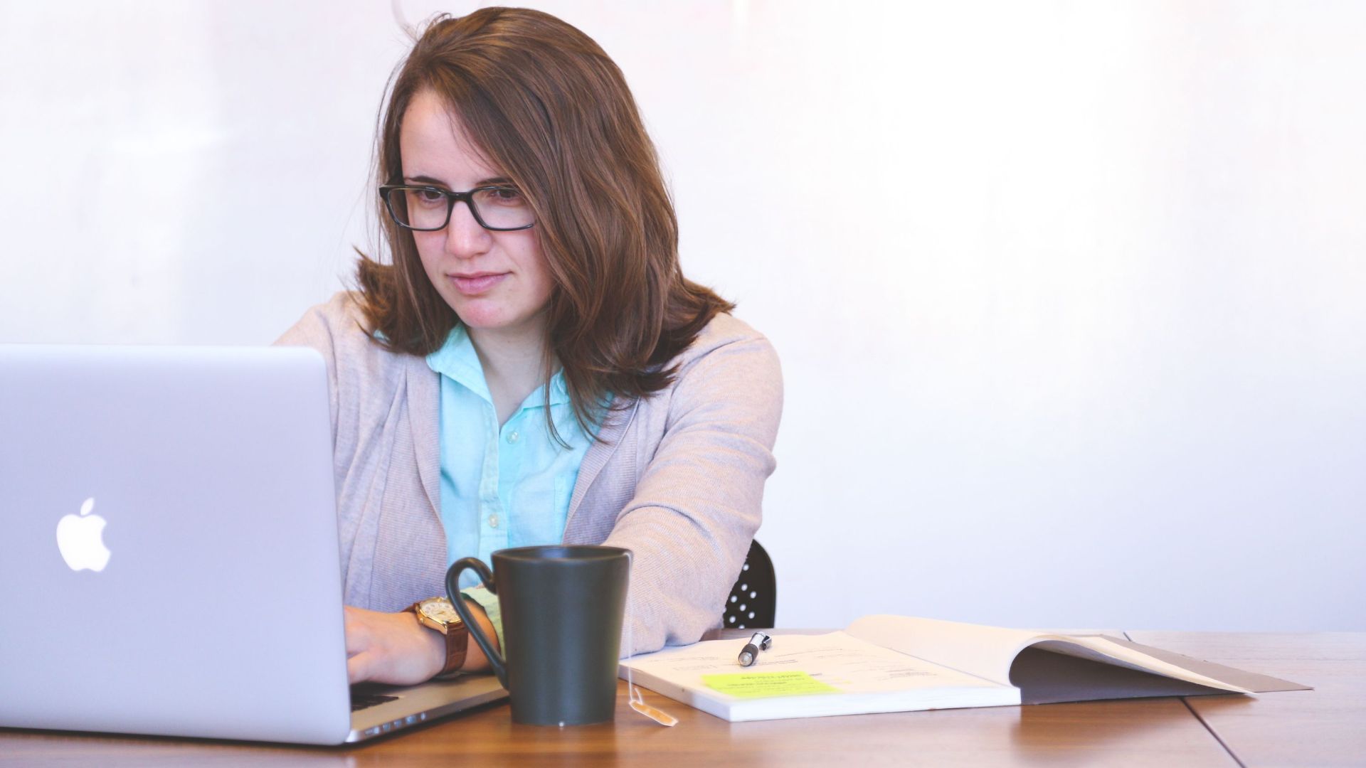 Focused businesswoman using a laptop at a desk with a mug and open notebook.