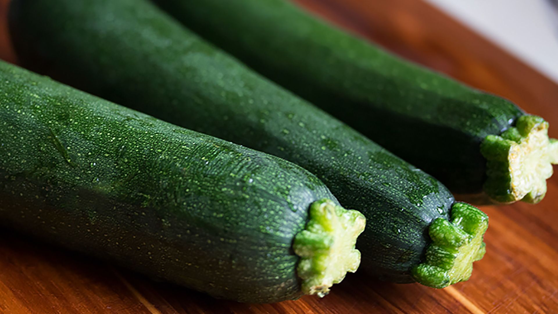 Close-up of three fresh green zucchinis on a wooden surface, perfect for food themes.