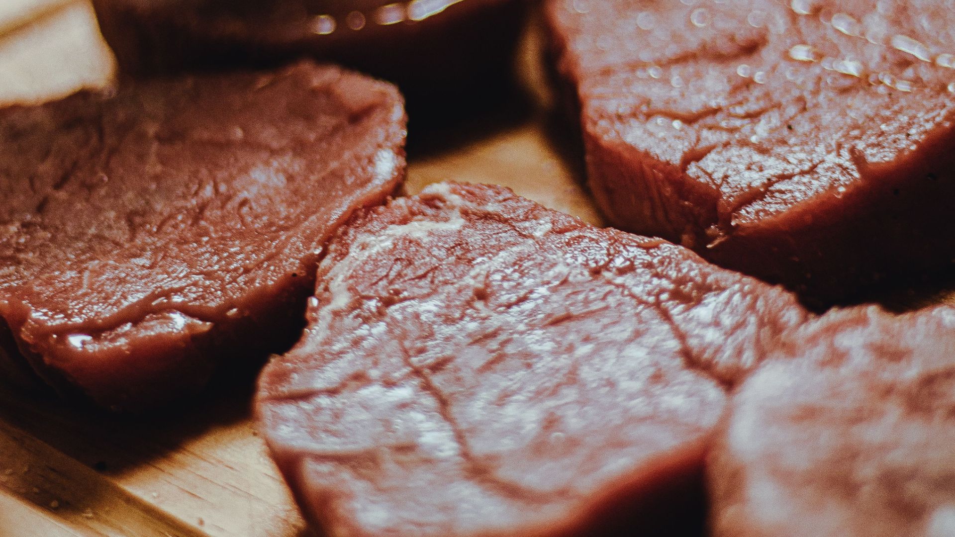 Fresh raw beef slices arranged on a wooden tray, ready for cooking.