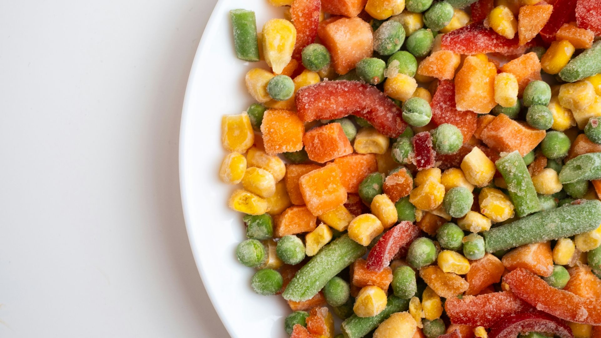A mix of frozen peas, corn, carrots, and green beans on a white plate