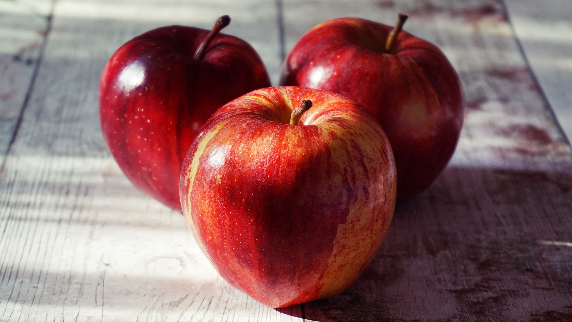 Close-up of fresh red apples on a rustic wooden table captured in natural light.