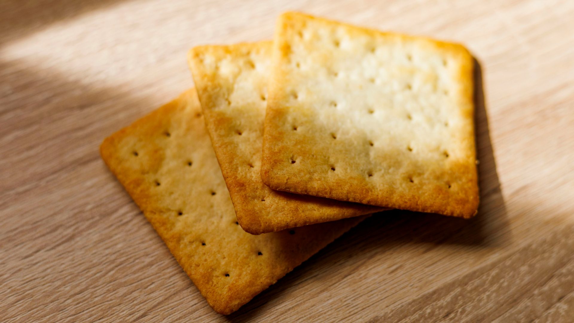 Three square crackers on a wooden table with sunlight