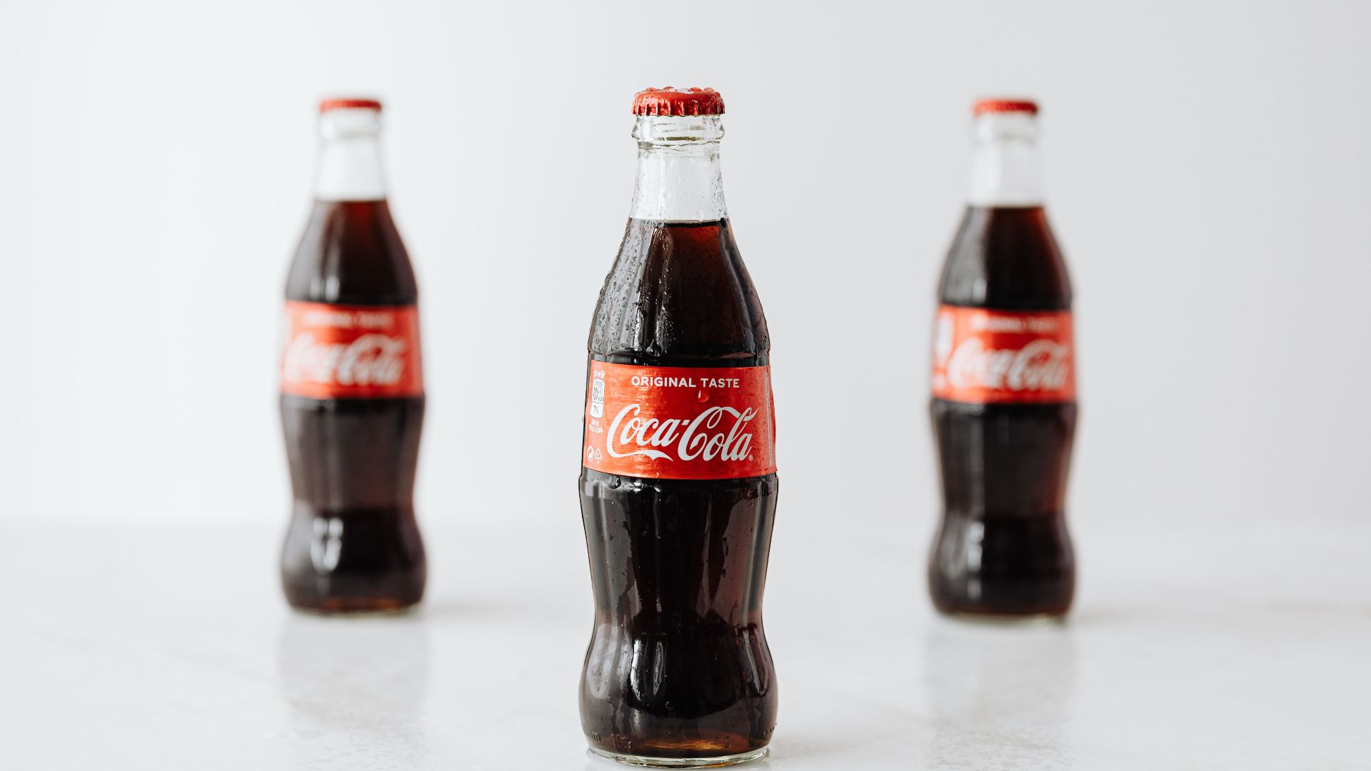 Modern glass bottles of cold soda with red label placed on white reflective surface